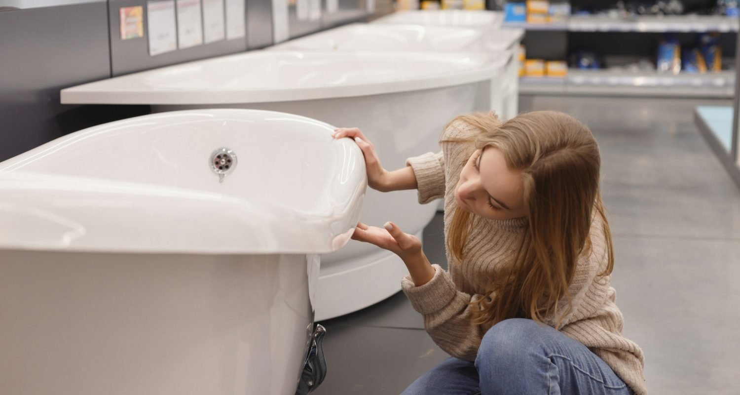 Woman choosing new acrylic bathtub in hardware store. Home bathroom renovation concept